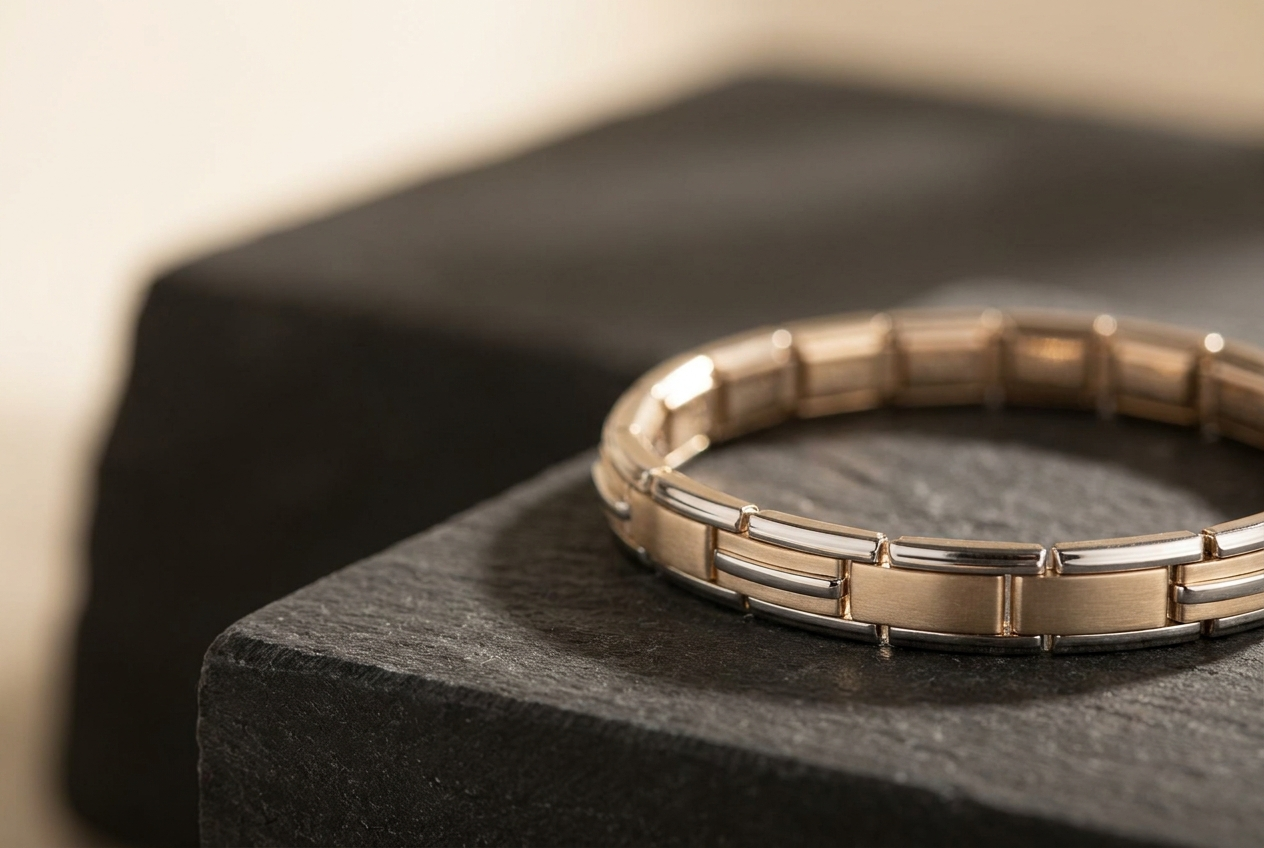 A champagne-gold TENLUMA bracelet resting on charcoal stone in warm light.